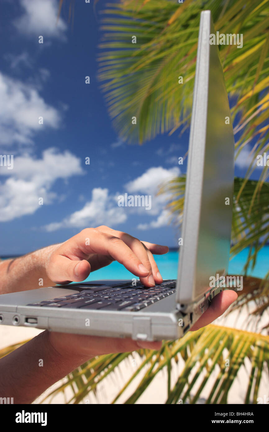A man's hands holding un ordinateur portable sur une plage tropicale Banque D'Images