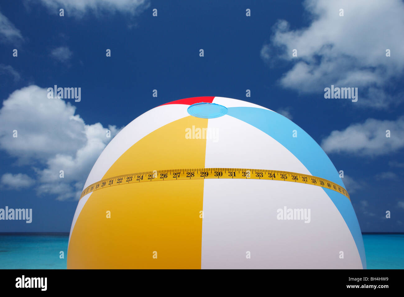 Un ruban de mesure enroulée autour d'un ballon de plage gonflable aux couleurs vives à l'encontre d'une mer bleue et le ciel tropical Banque D'Images
