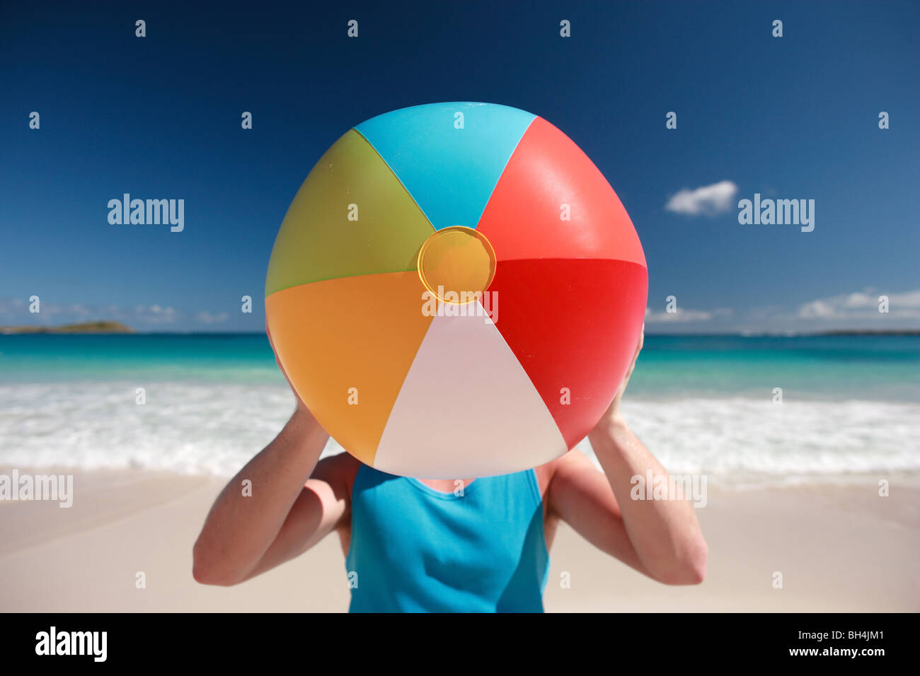 Jeune homme tenant un ballon de plage gonflable sur son visage sur une plage tropicale déserte Banque D'Images