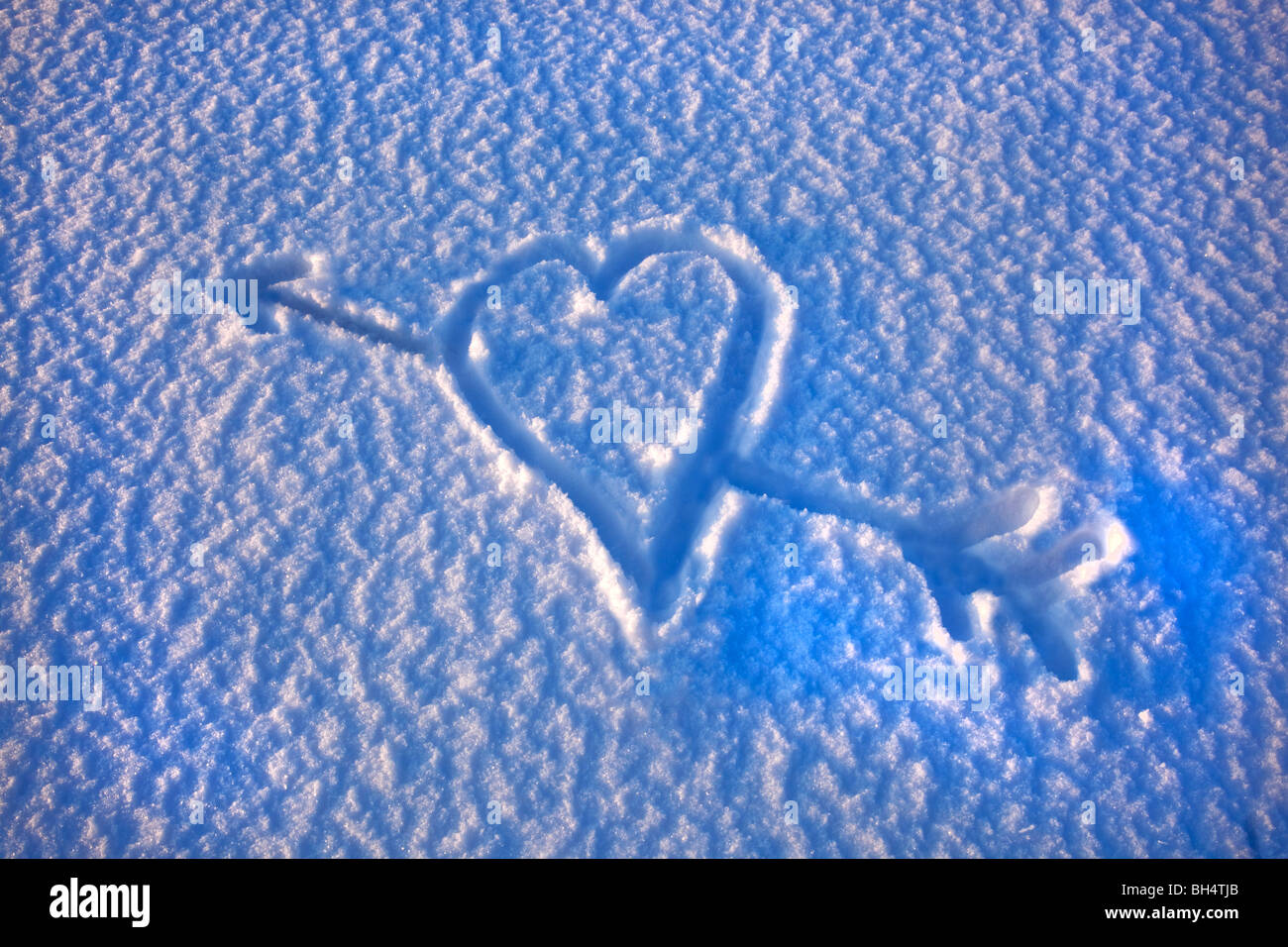 Un coeur d'amour avec la flèche de Cupidon à travers elle dessiné dans la neige Banque D'Images