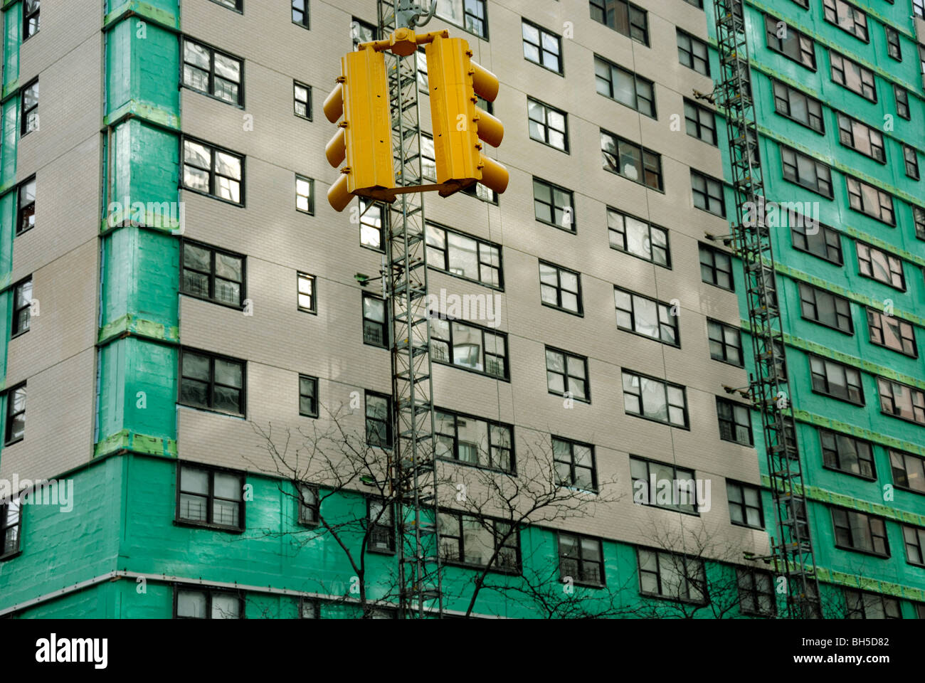 Un feu de circulation est à l'opposé d'un immeuble à appartements drapée de matière verte. Banque D'Images