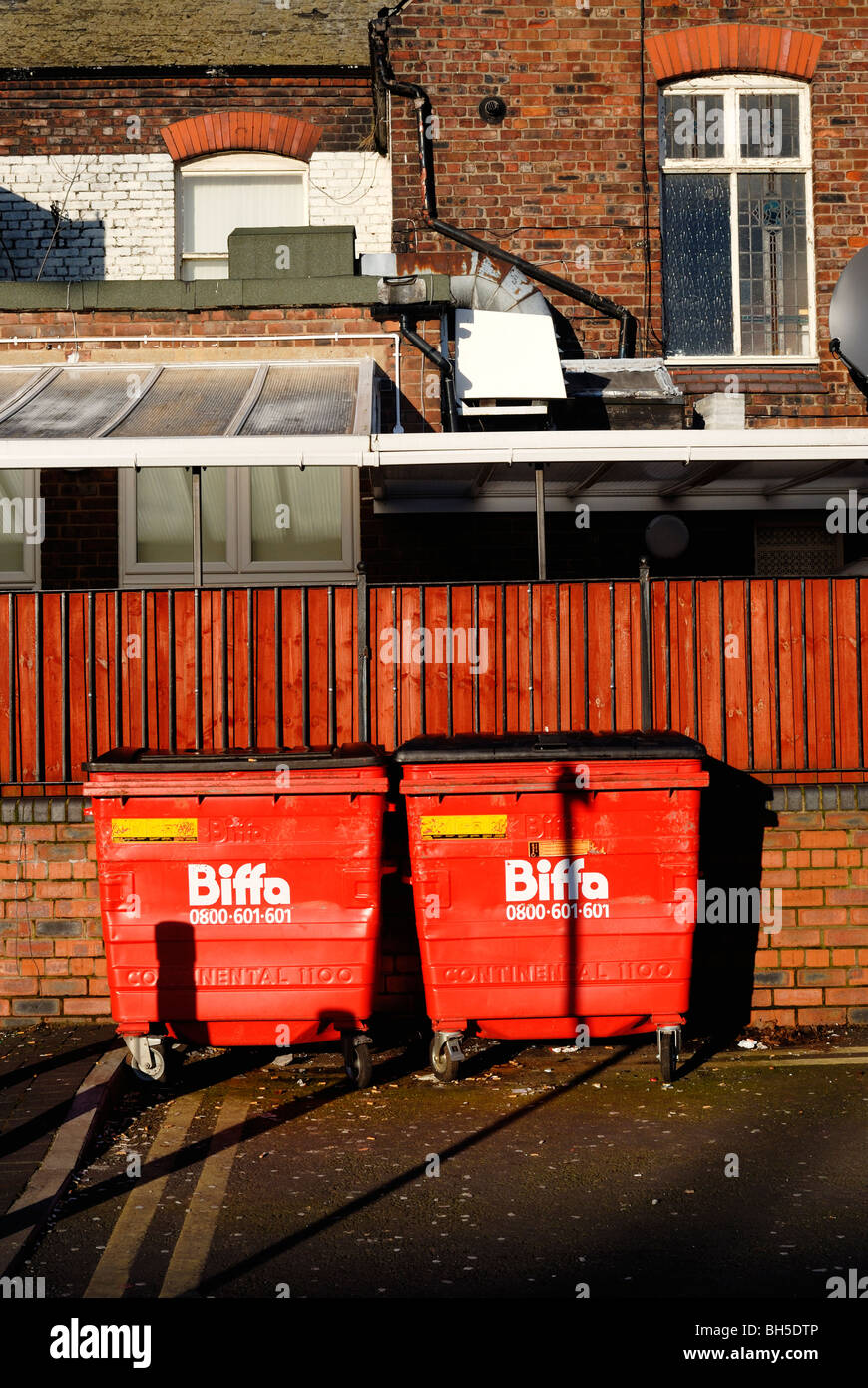 Wheelybins Biffa rouge vif derrière des locaux commerciaux à Widnes, Cheshire. Banque D'Images