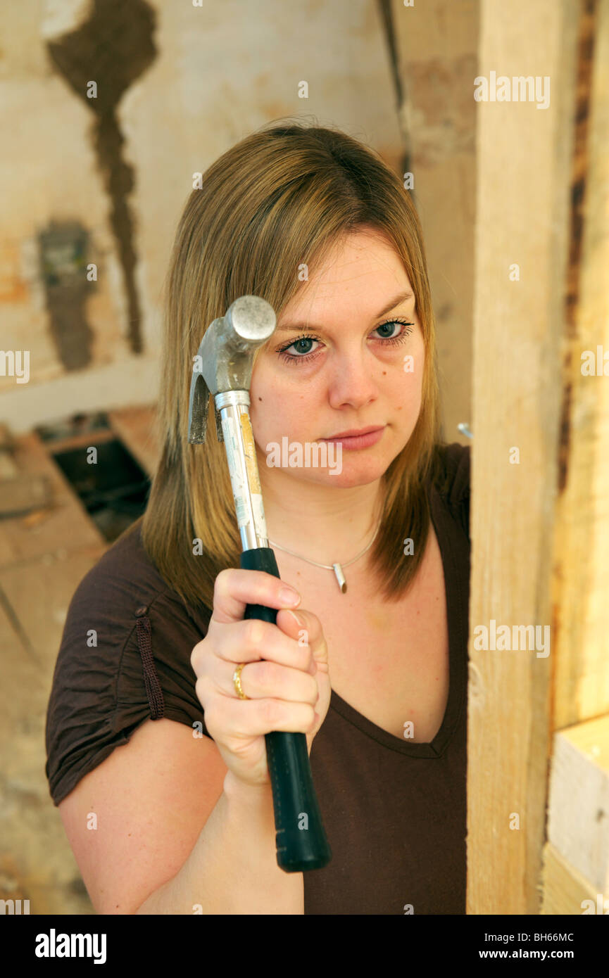 Jeune femme frapper un clou avec un marteau au cours de projet de bricolage Banque D'Images