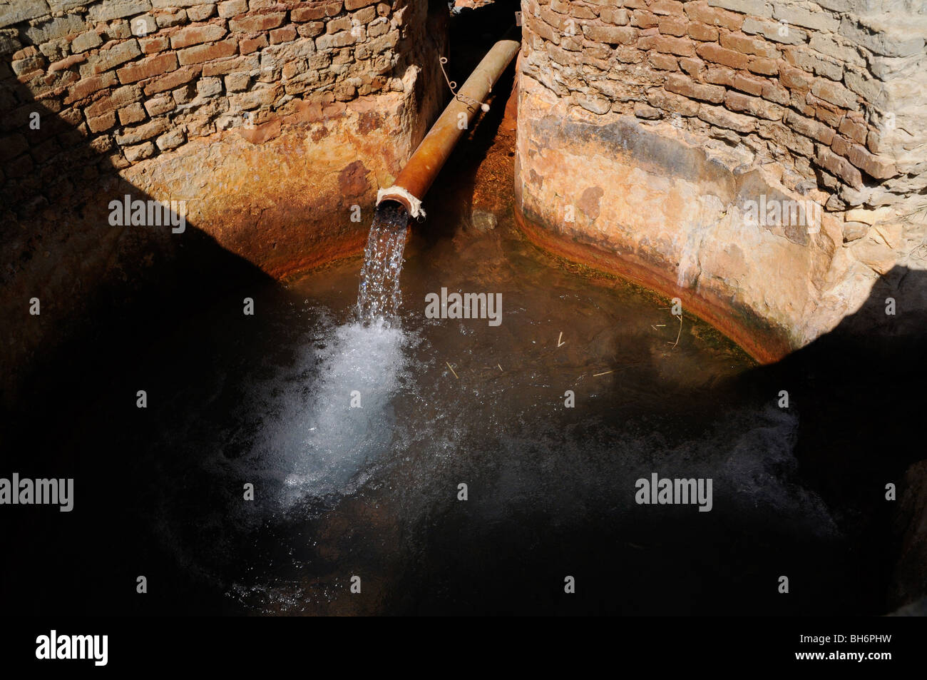 L'eau s'écoulant des sources chaudes s'écoule dans un puits d'irrigation en briques profondes sur une ferme à Qasr Farafra, dans l'oasis de Farafra au Sahara, dans le désert occidental, en Égypte Banque D'Images