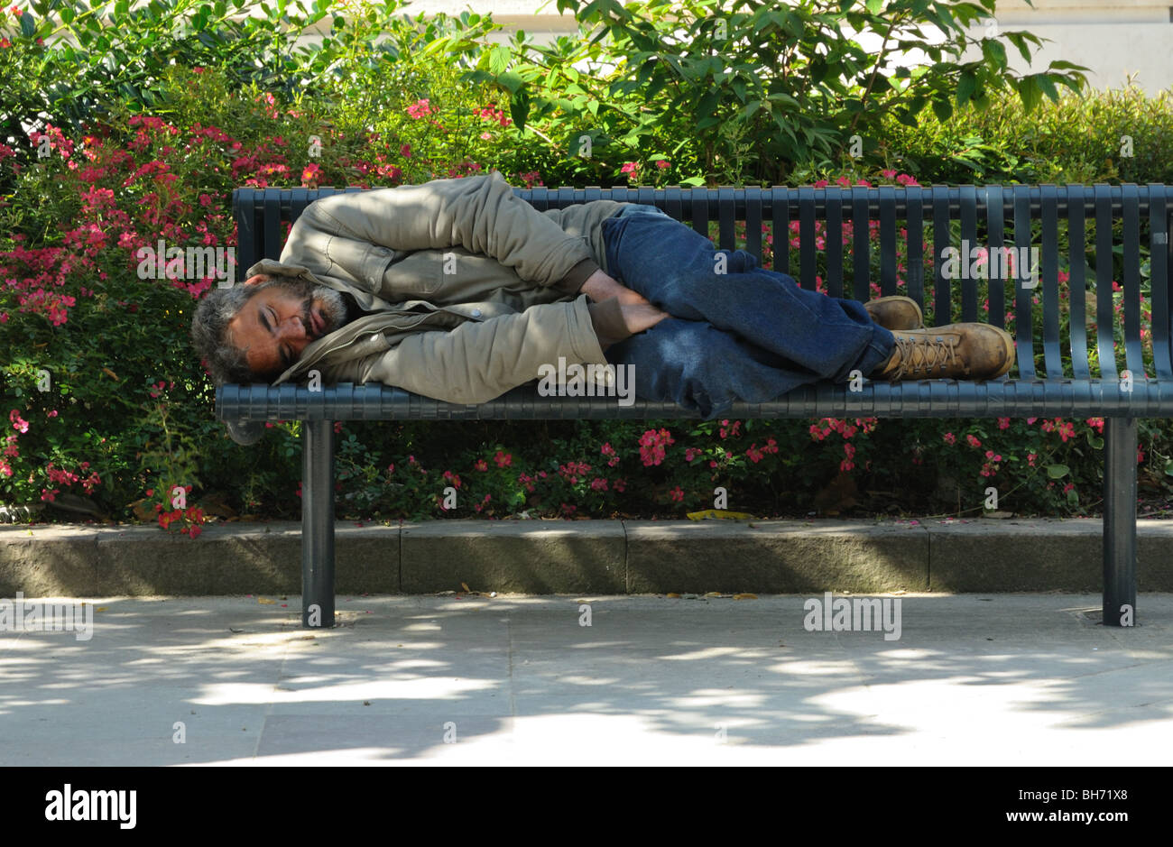 Un sans-abri dormant sur un banc public dans un parc de la ville Banque D'Images