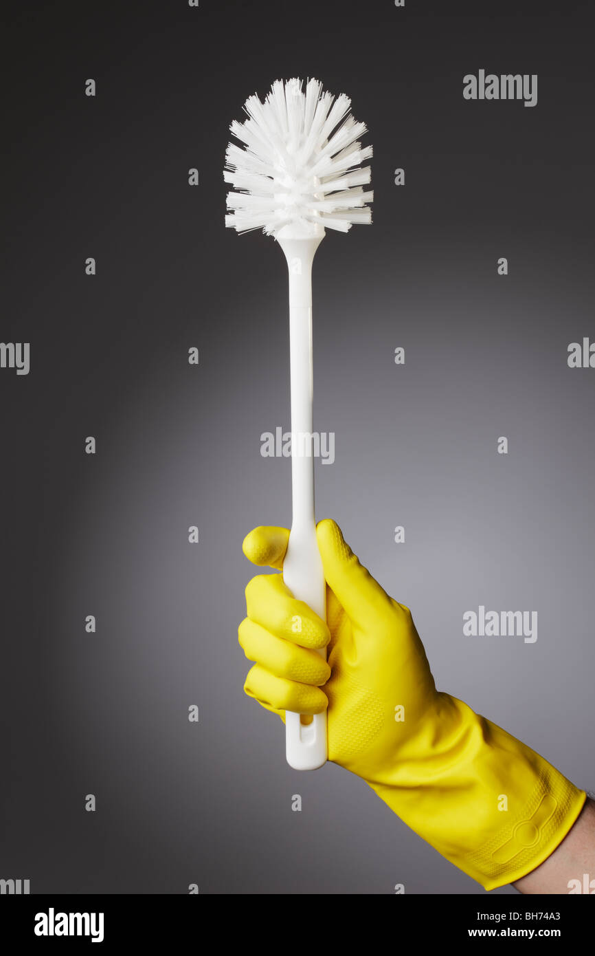 Une main gantée tenant une brosse de toilettes propres Banque D'Images
