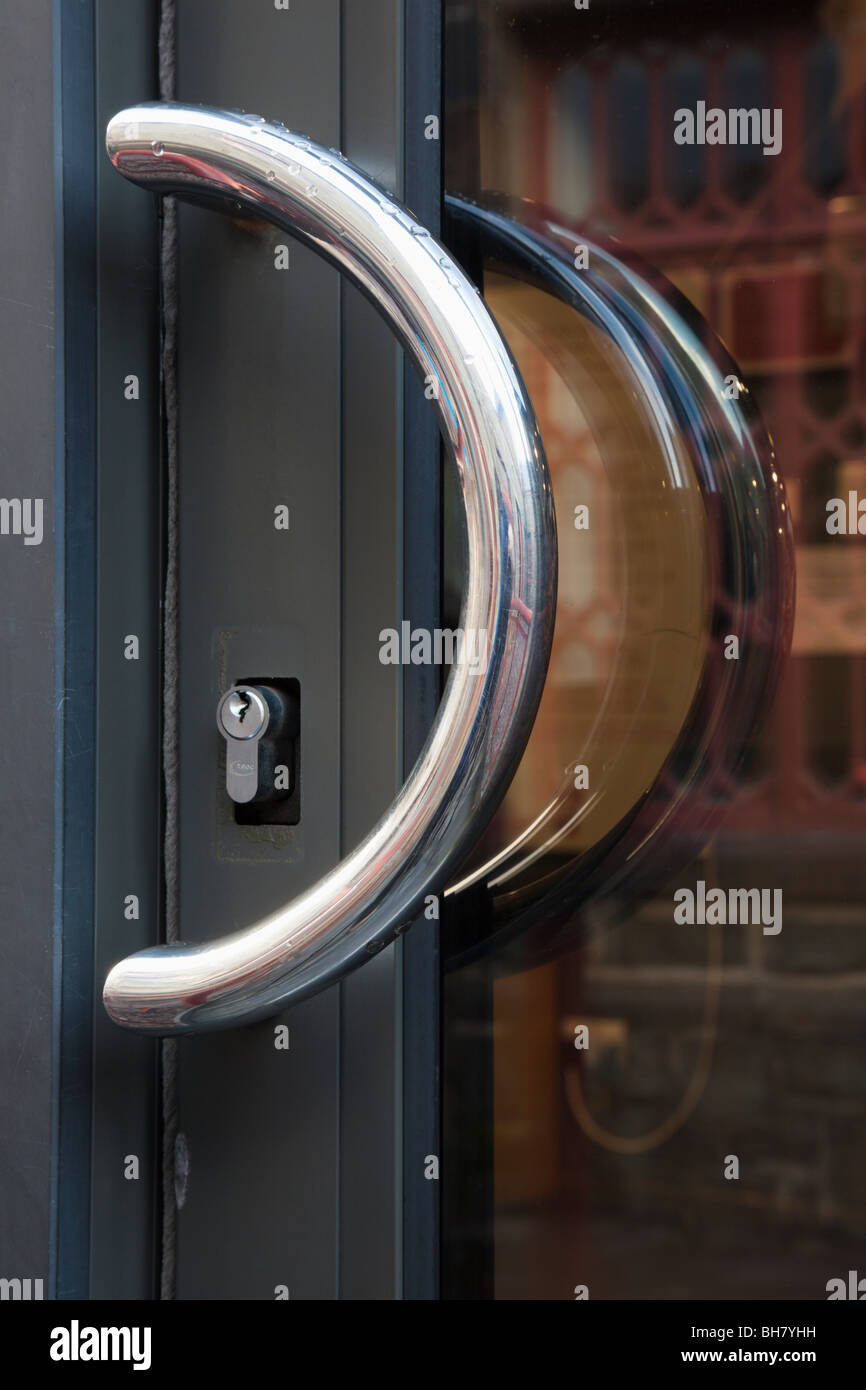 Close-up d'une poignée chromée semi-circulaire et serrure sur une porte en verre Banque D'Images