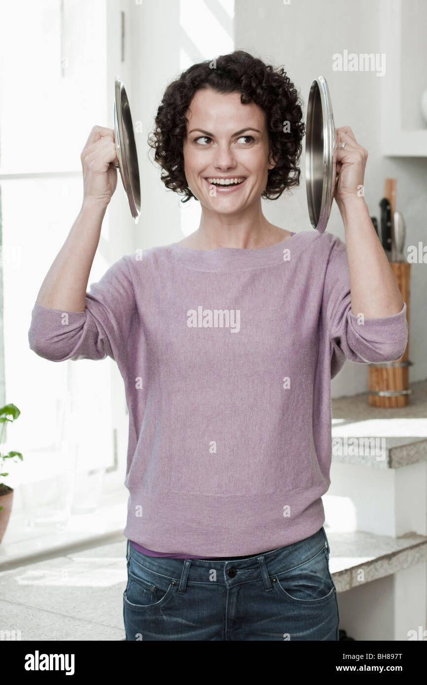 Une femme tenant deux couvercles pan à ses oreilles Banque D'Images