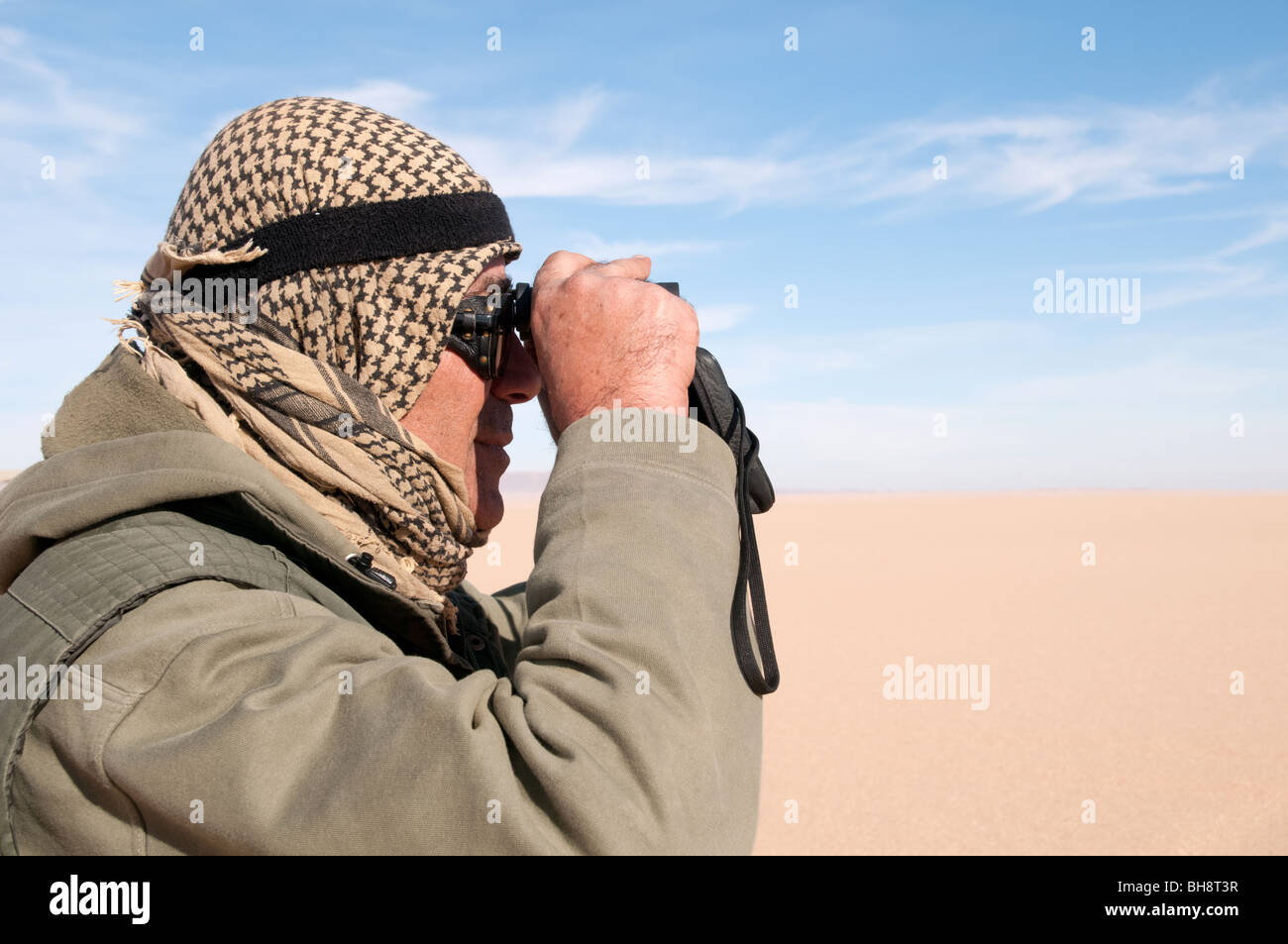 Un guide saharien regarde à travers ses jumelles vers les dunes de sable dans le Gilf Kebir région du désert occidental, dans le sud-ouest de l'Égypte. Banque D'Images