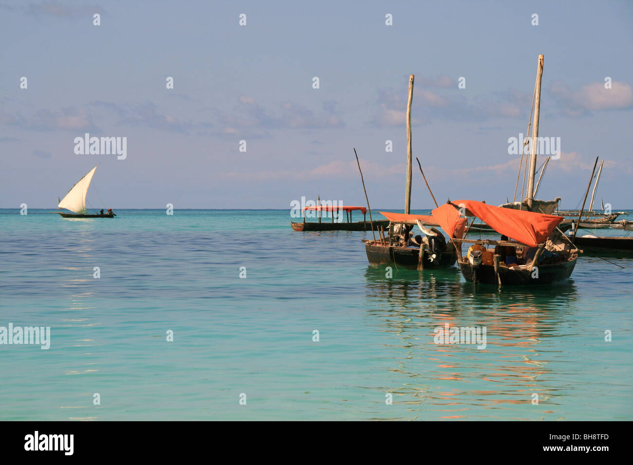 Les pêcheurs à l'abri du soleil sous la toile rouge à bord de leurs bateaux de pêche en bois au large plage de Nungwi, Zanzibar. Banque D'Images