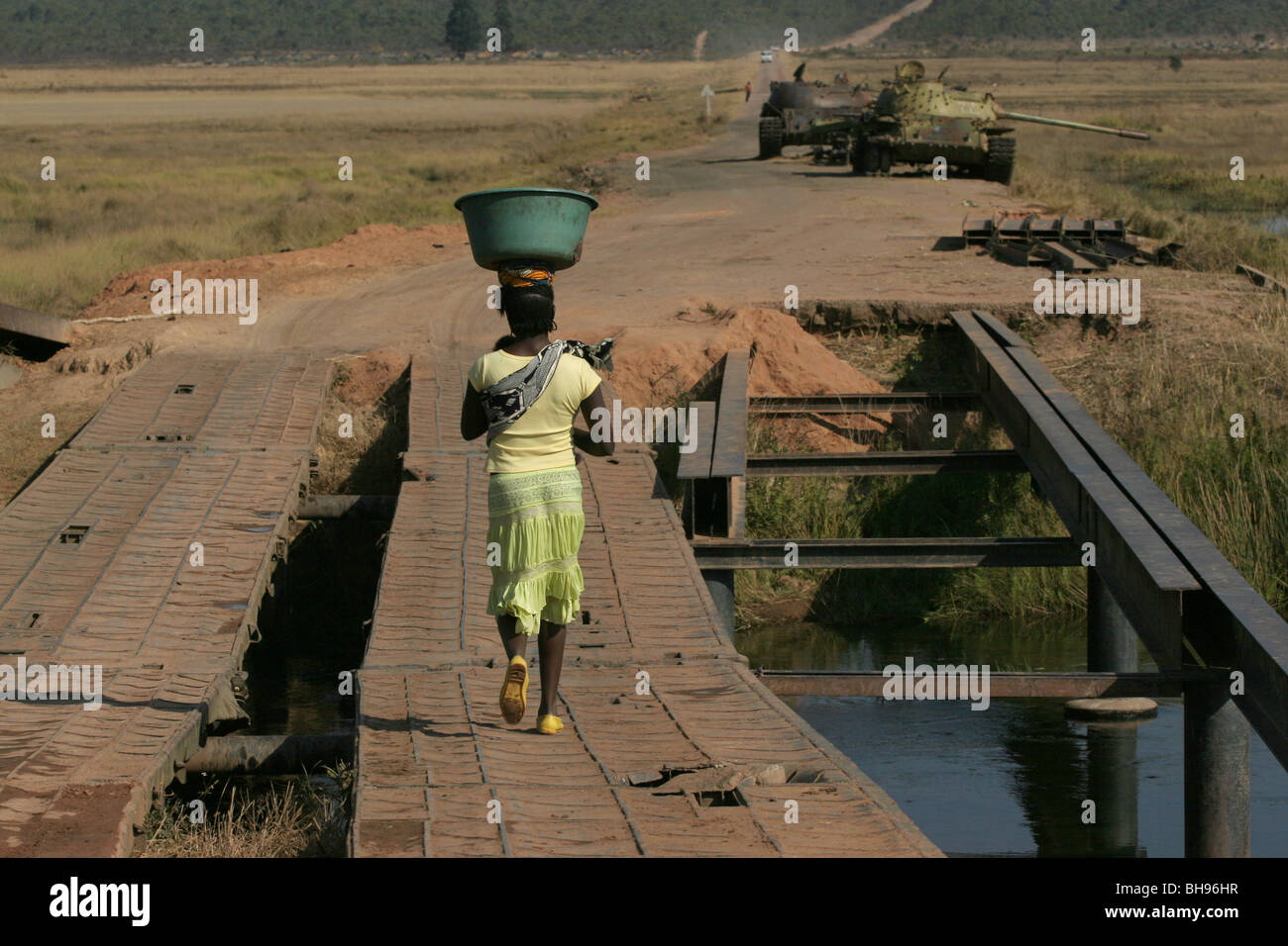 Femme angolaise exerçant son panier sur sa tête se dirige vers deux réservoirs qui ont été abandonnés à Longa, l'Angola, l'Afrique. Banque D'Images