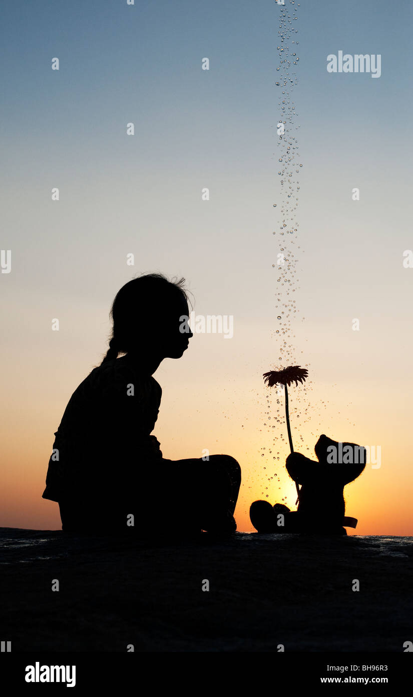 Indian girl et ours tient une fleur au coucher du soleil avec des gouttes d'eau. Silhouette. L'Inde Banque D'Images