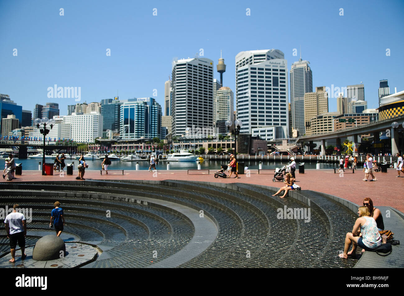 Fontaine en spirale de Darling Harbour enfants jouant Sydney // SYDNEY, Australie — enfants jouant dans la fontaine en spirale de Darling Harbour par une chaude journée d'été. La zone dynamique du front de mer est animée par l'activité, offrant une évasion rafraîchissante de la chaleur au milieu des gratte-ciel de la ville. Banque D'Images