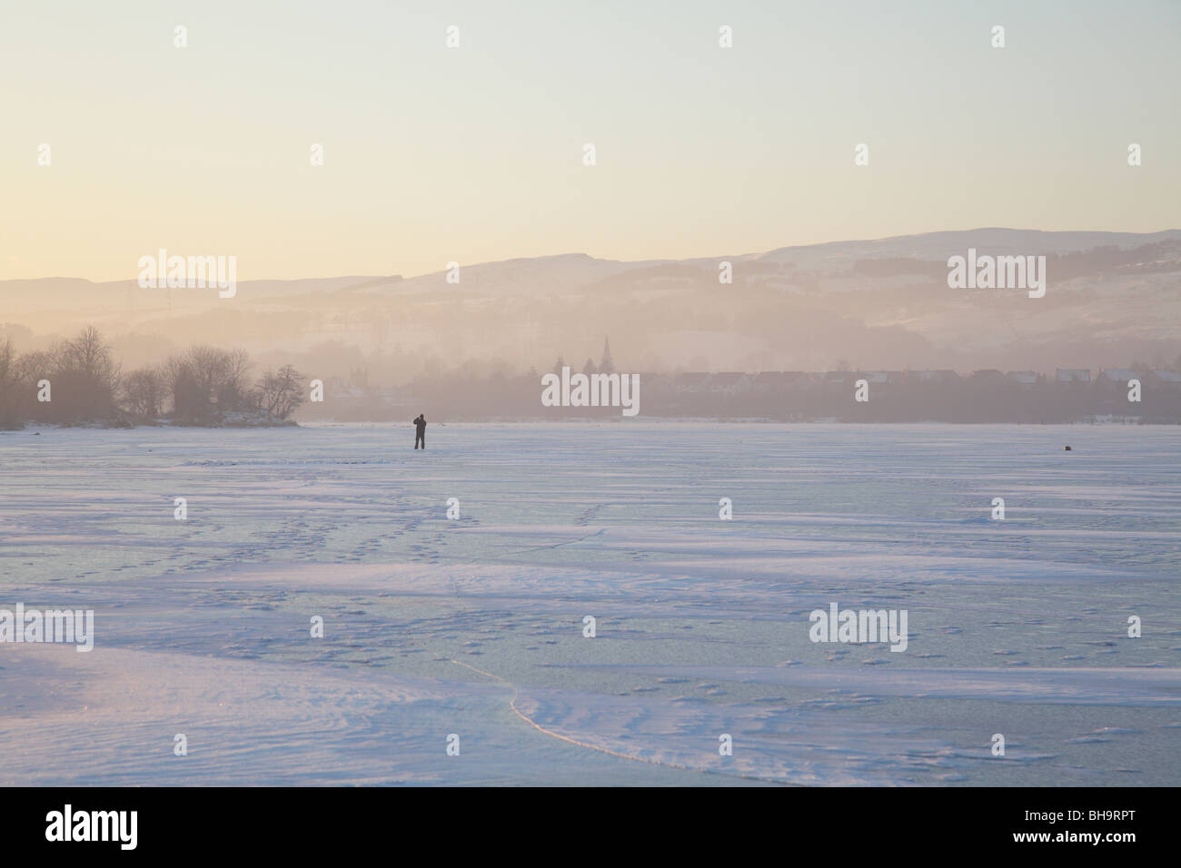 Homme marchant sur un château gelé Semple Loch en hiver, Parc régional de Clyde Muirshiel, Lochwinnoch, Renfrewshire, Écosse, Royaume-Uni Banque D'Images