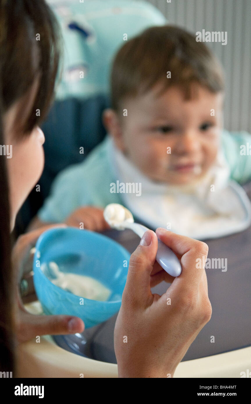 Jeune femme nourrir bébé garçon dans une chaise haute Banque D'Images