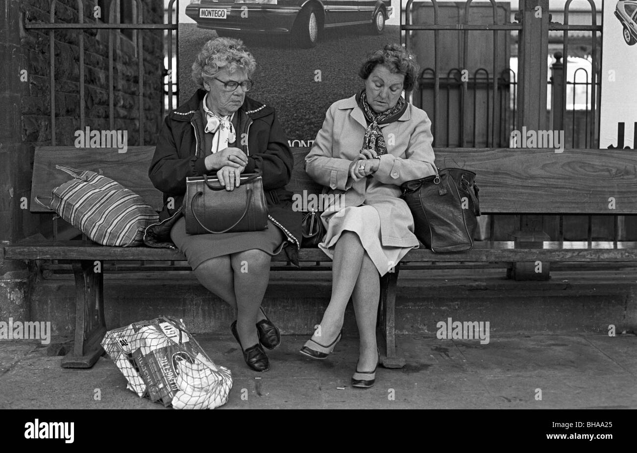 Après le magasinage, deux dames vérifier l'heure sur leurs montres dans l'attente d'un train à la gare de Newport, Pays de Galles Banque D'Images