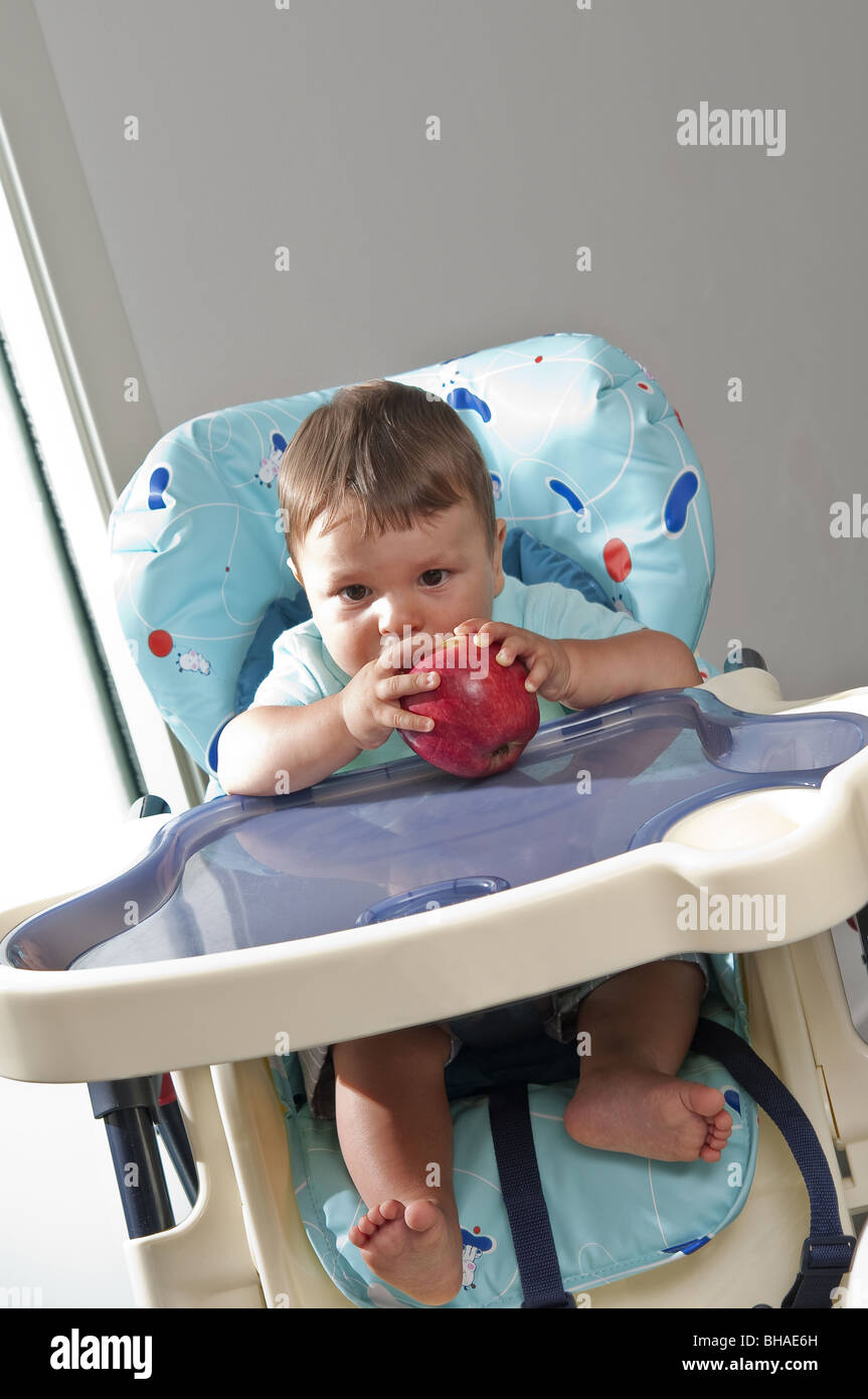 Chaise haute Bébé garçon en tenant une pomme Banque D'Images