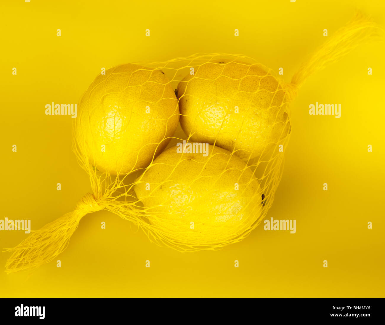 Trois citrons jaunes dans une chaîne-sac sur un fond jaune. Banque D'Images