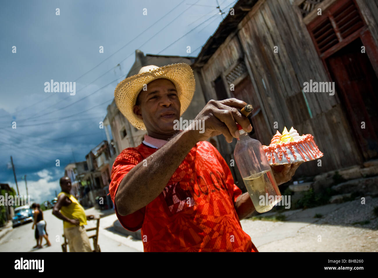 Un homme qui se précipitait pour un cubain fiesta, tenant une bouteille de rhum, fumer un cigare et de transporter un gâteau, à Santiago de Cuba, Cuba. Banque D'Images
