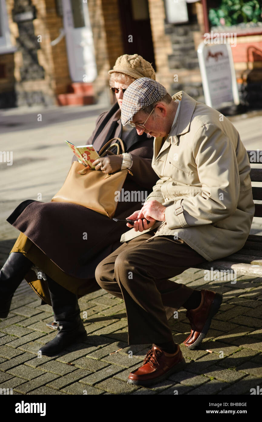 Homme âgé saisie des contacts dans son téléphone mobile comme son épouse de leur lecture de son carnet d'adresses, UK Banque D'Images