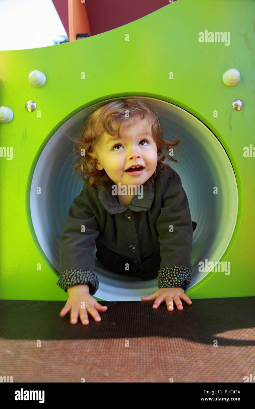Une petite fille de vingt mois jouant sur une diapositive dans un jardin public Banque D'Images