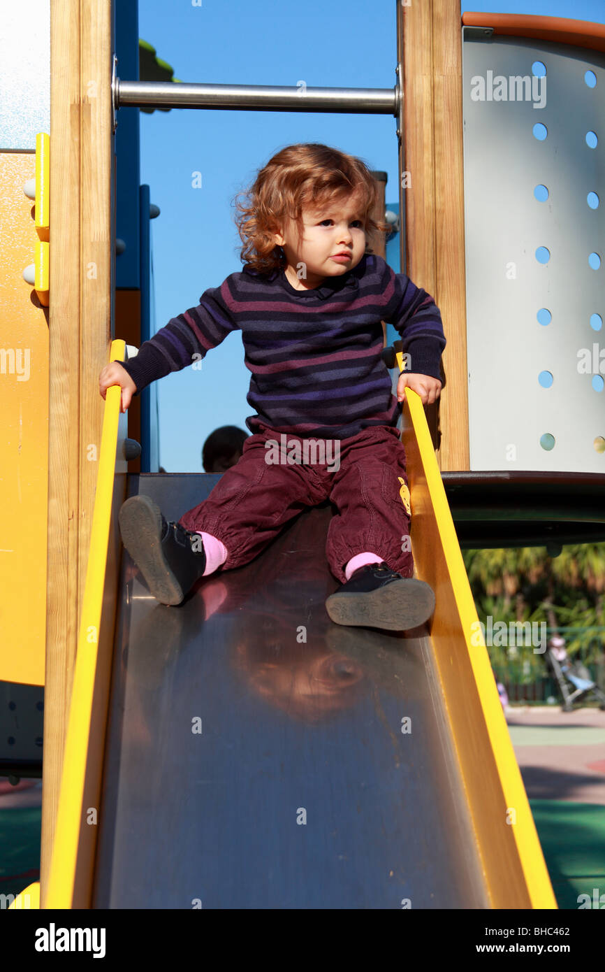 Une petite fille de vingt mois jouant sur une diapositive dans un jardin public Banque D'Images