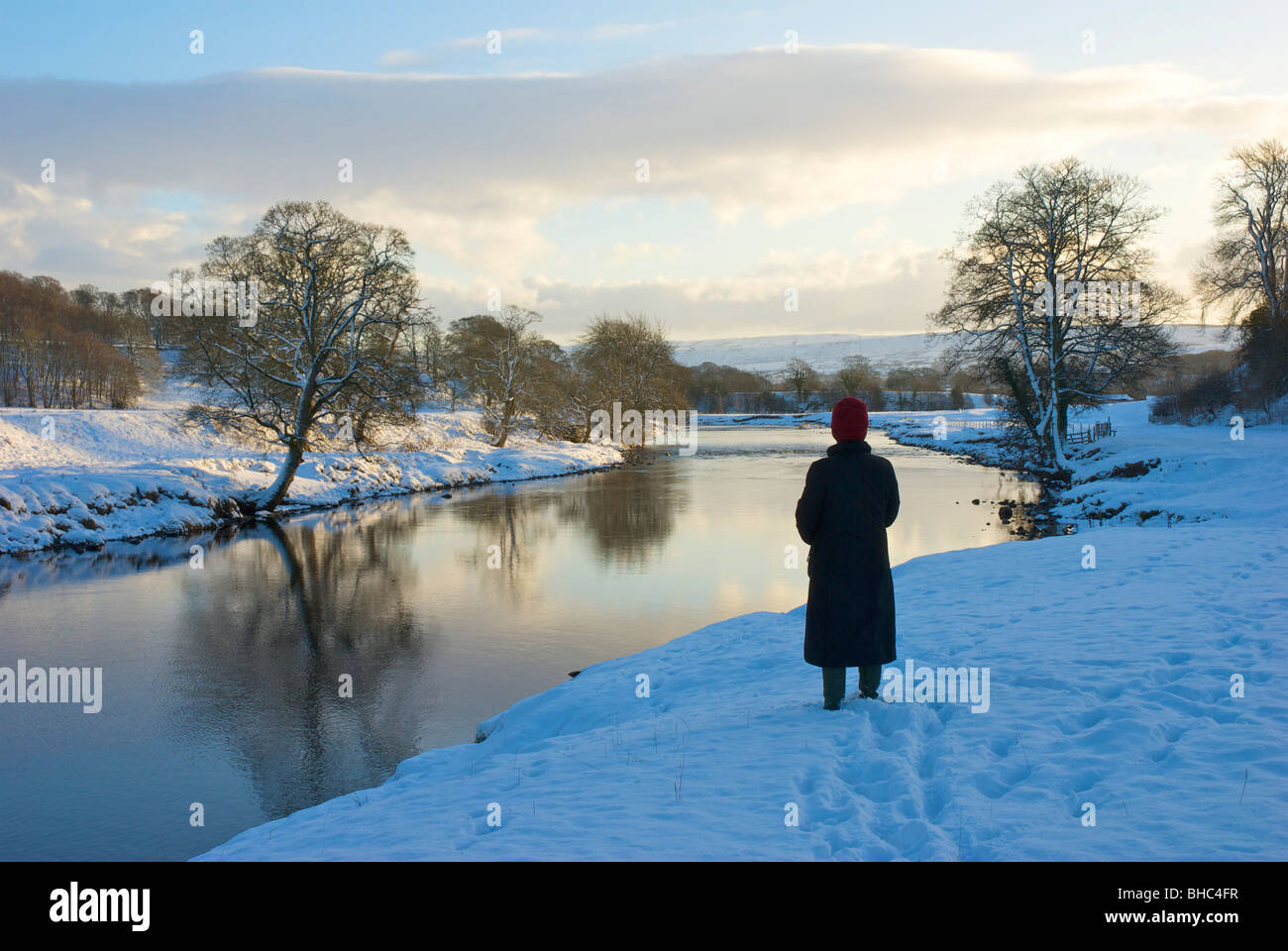 Woman standing by River Wharfe près de Saint-cergue en hiver, Wharfedale, North Yorkshire, England UK Banque D'Images