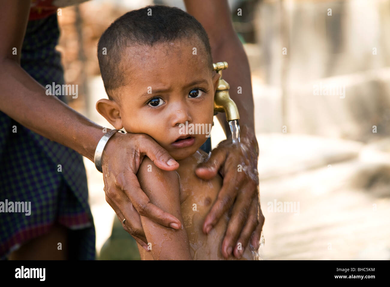 Bébé garçon d'être lavés sous l'eau du robinet nouvellement installé pour la première fois dans le camp de personnes déplacées à Dili, Timor Oriental Banque D'Images