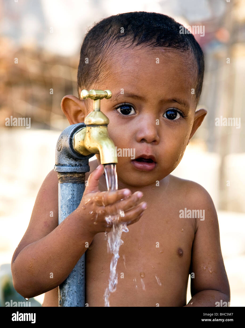 Bébé garçon nouvellement installé à l'aide de l'eau du robinet à un IDP camp de personnes déplacées à Dili au Timor oriental Banque D'Images