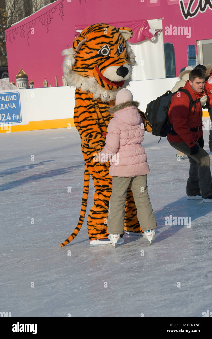 Une petite fille avec un homme habillé en costume de tigre sur la patinoire Banque D'Images