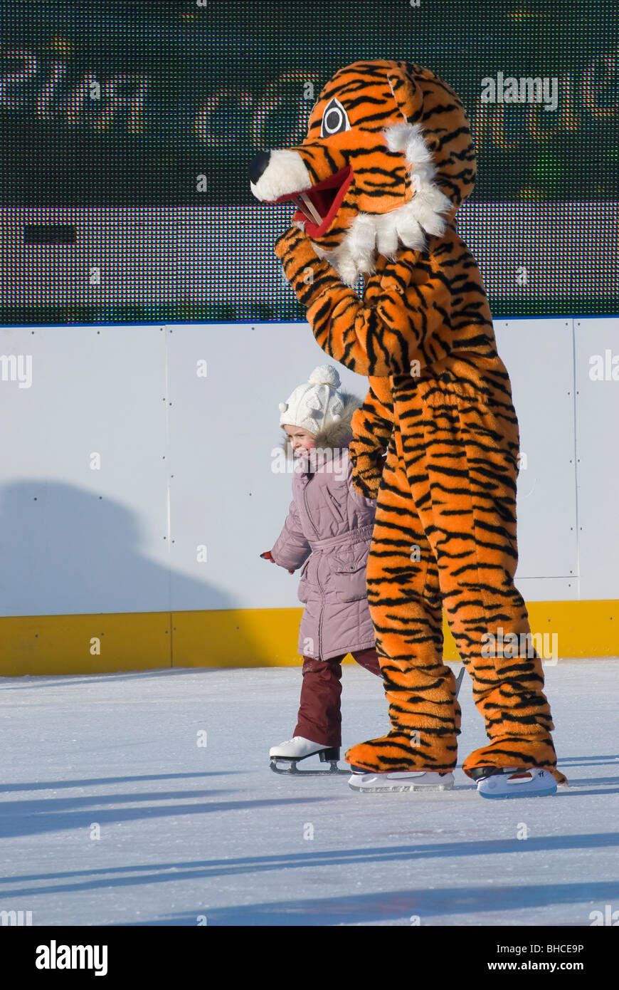 Une petite fille avec un homme habillé en costume de tigre sur la patinoire Banque D'Images