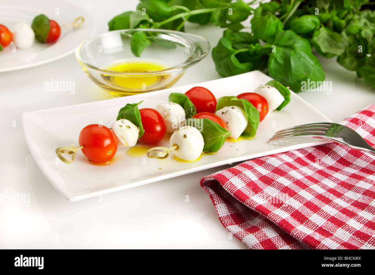 Salade caprese - spitted tomates cerise, boules de mozzarella et les feuilles de basilic sur une plaque rectangulaire, avec de l'huile d'olive raffinée Banque D'Images