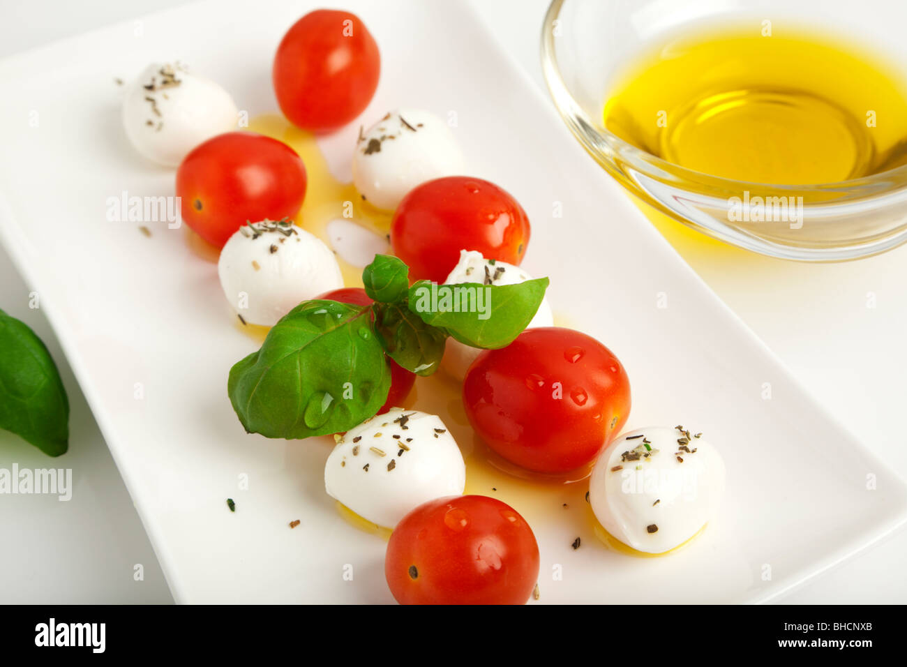 Boules de fromage mozzarella spitted aux tomates et les feuilles de basilic avec l'huile d'olive herbes nad sur une plaque Banque D'Images