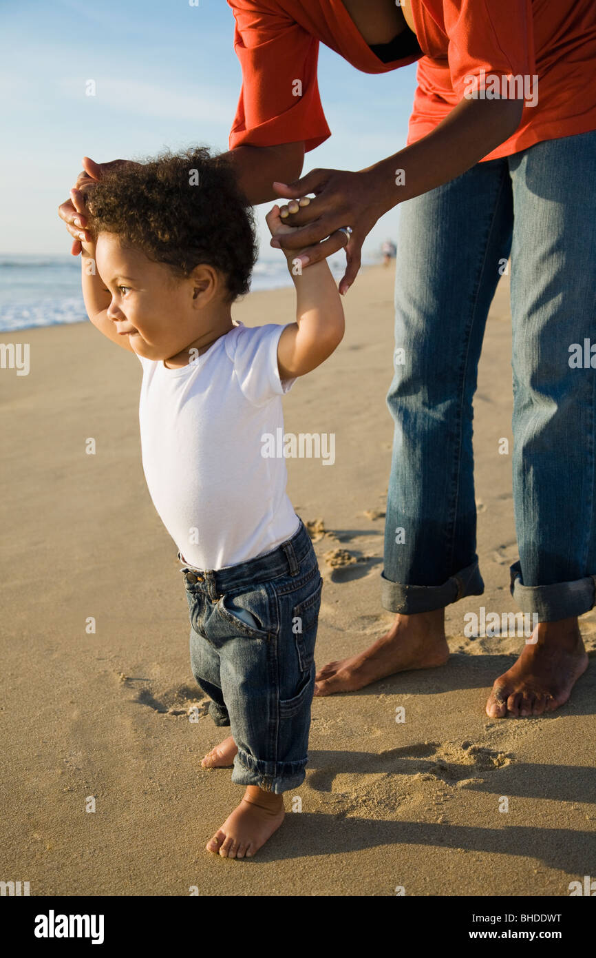 Mère de l'Afrique aidant fils à pied à la plage Banque D'Images