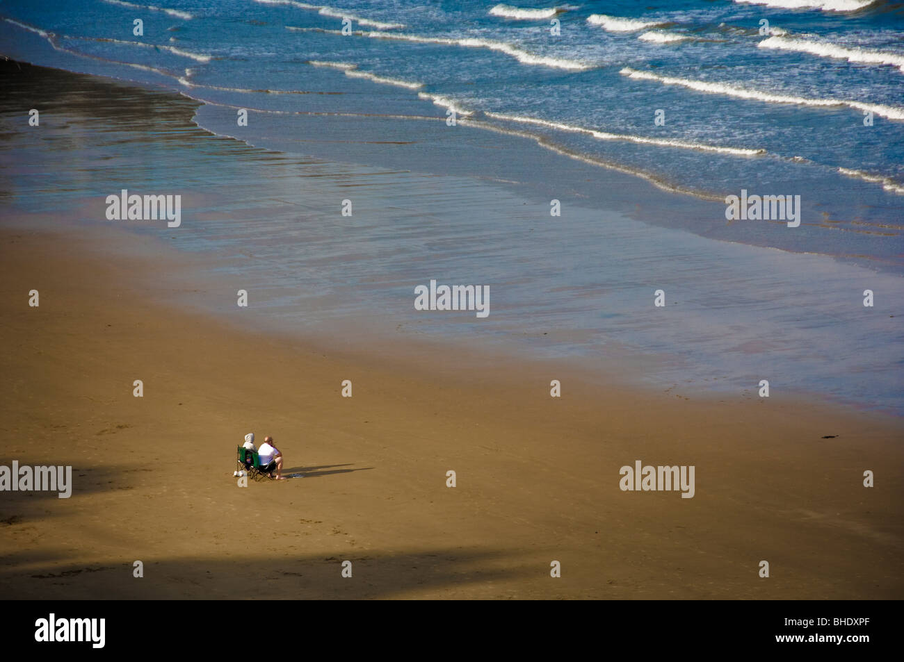 Vue arrière d'un couple adulte non identifiable, assis sur des chaises pliantes sur une plage britannique déserte, avec vue sur la mer. Banque D'Images
