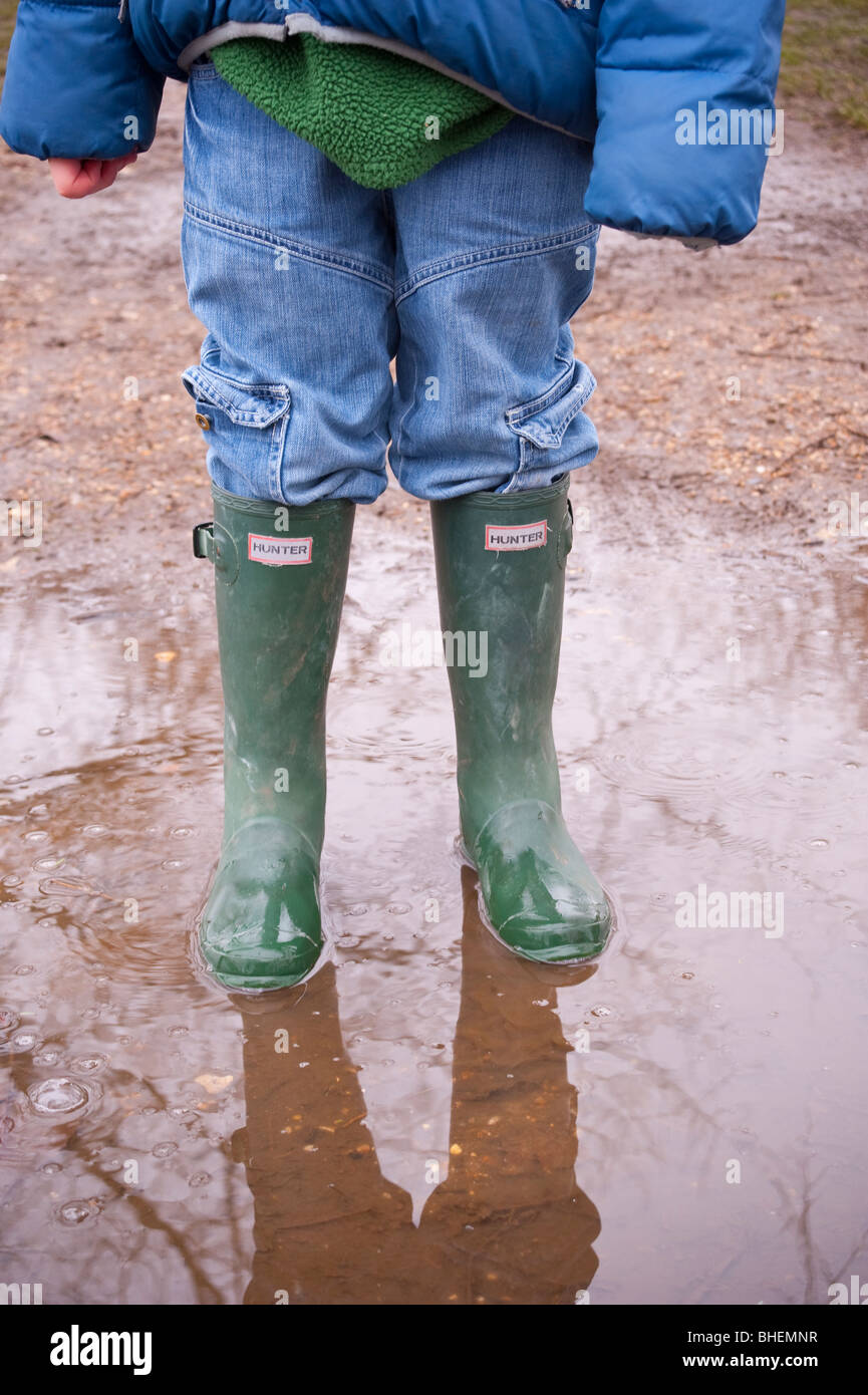 Un garçon se tient dans une flaque d'eau portant des bottes wellington Hunter au Royaume-Uni Banque D'Images