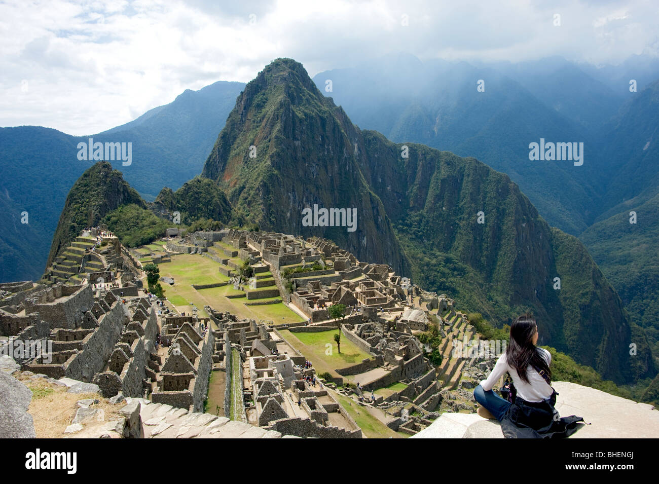Une femme assise sur une saillie rocheuse à admirer la vue sur le Machu Picchu et la zone environnante, Pérou Banque D'Images