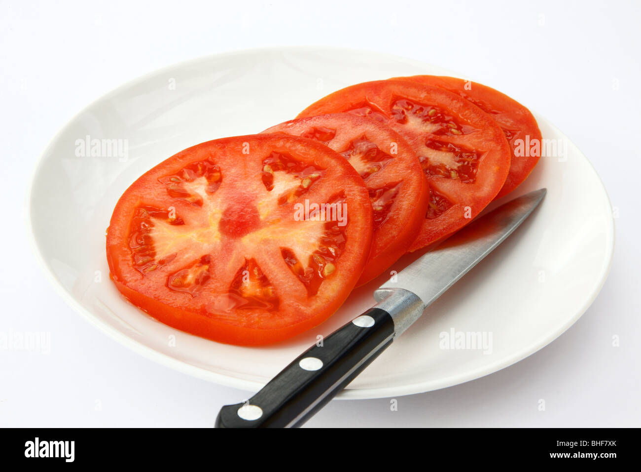 Meubles de grand, mûr, juteux, rouge tomates sur une plaque blanche avec couteau de cuisine. Banque D'Images