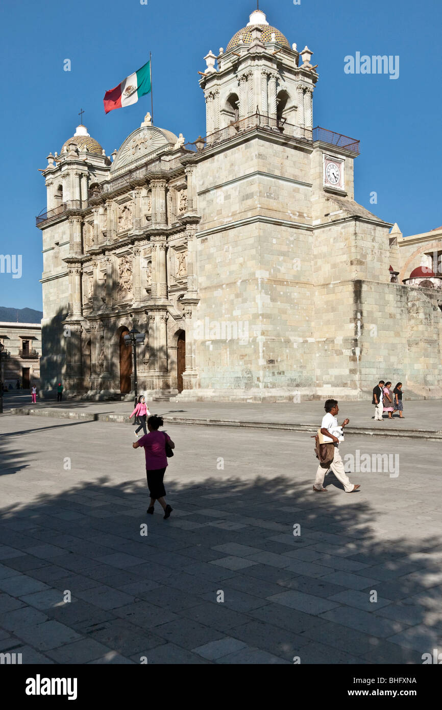Les gens se promener par l'ombre de la ville d'Oaxaca avant pommelé Cathédrale comme drapeau mexicain vole jauntily entre ses tours Banque D'Images