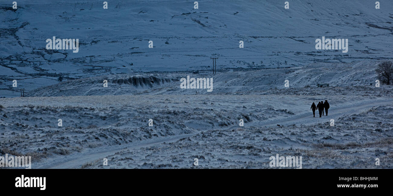 Quatre personnes à pied sur route enneigée au crépuscule sur le Blorenge moorland en hiver Wales UK Banque D'Images