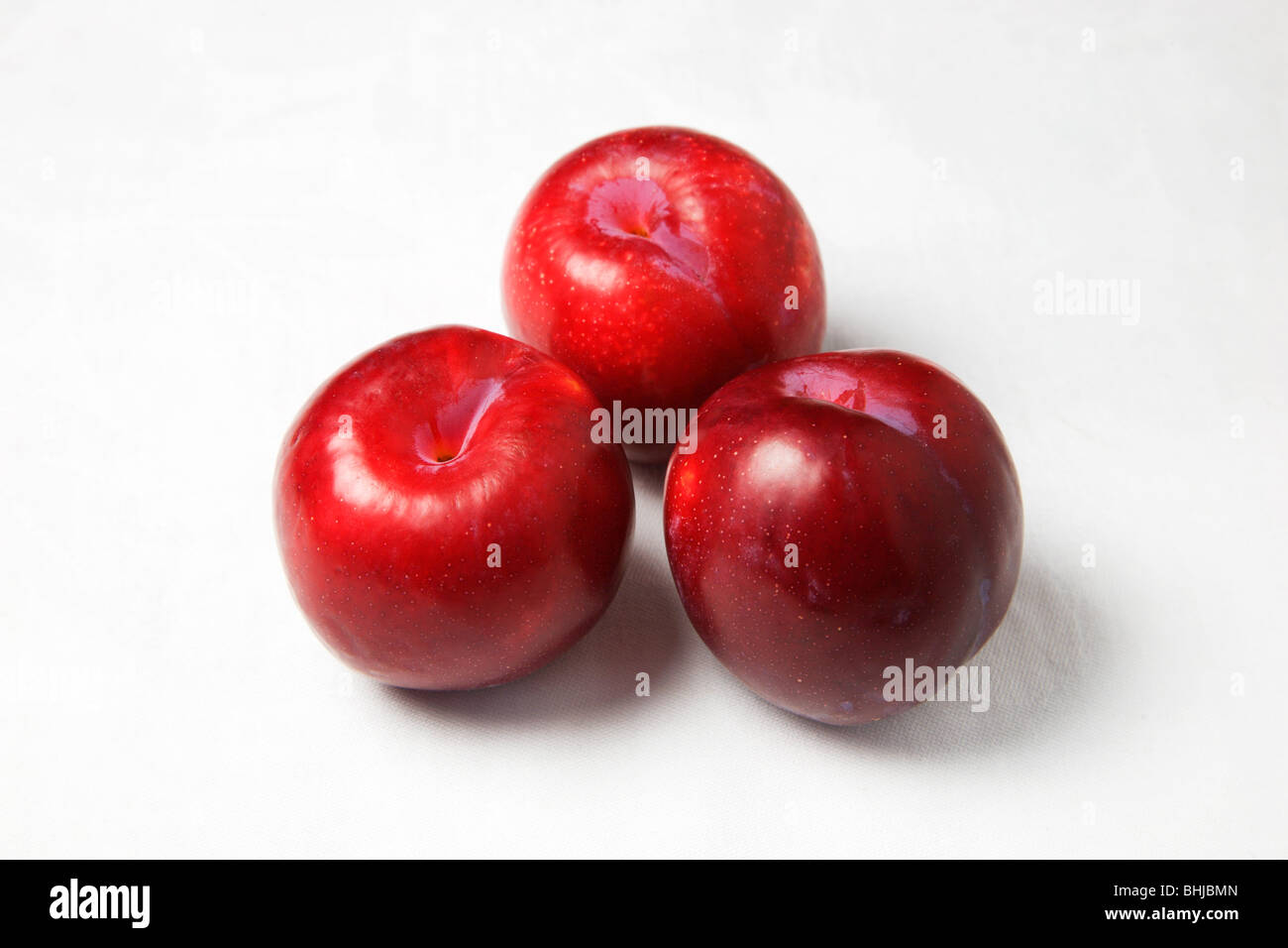 Trois prunes rouges sur un fond blanc Banque D'Images