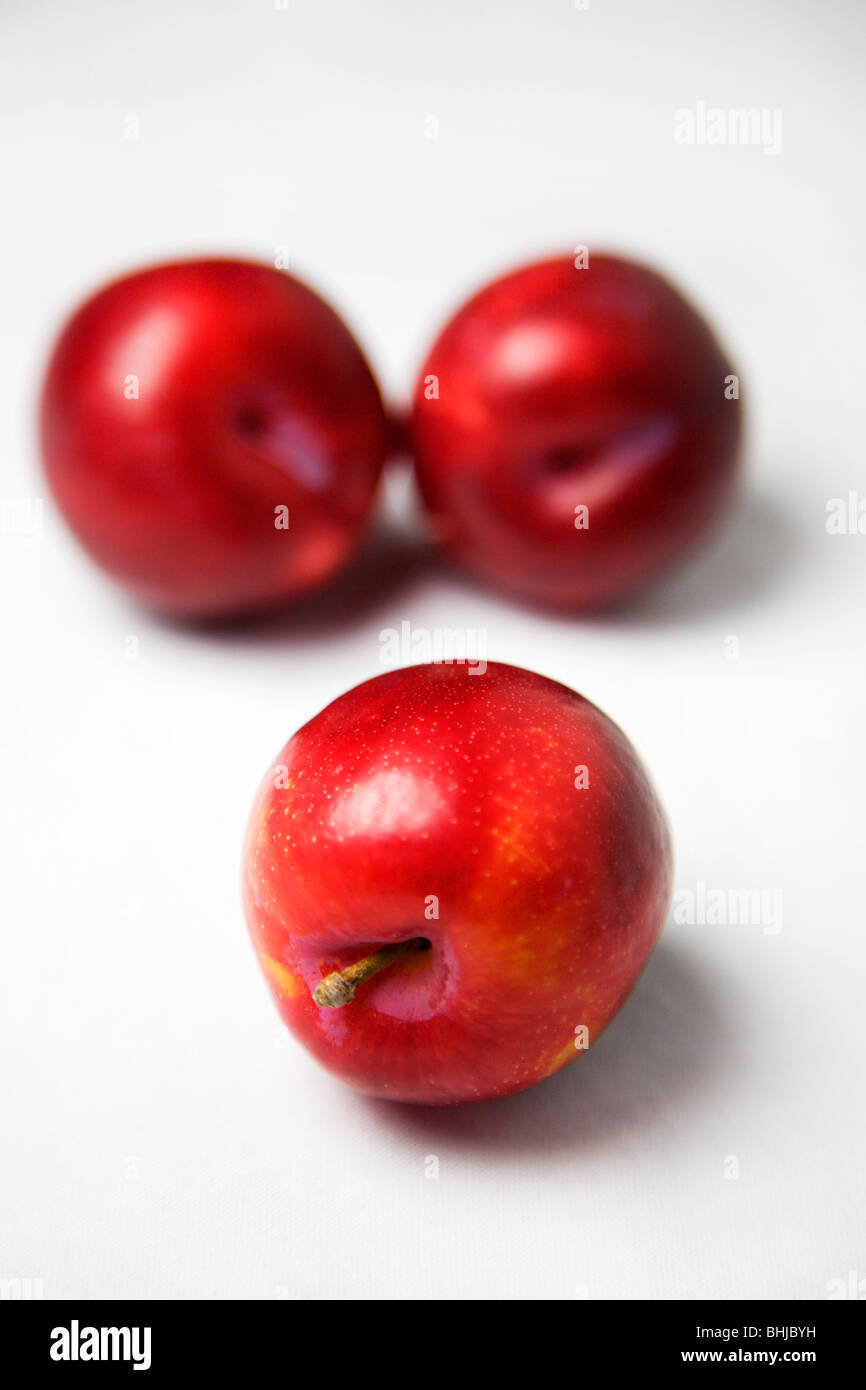 Trois prunes rouges sur un fond blanc Banque D'Images