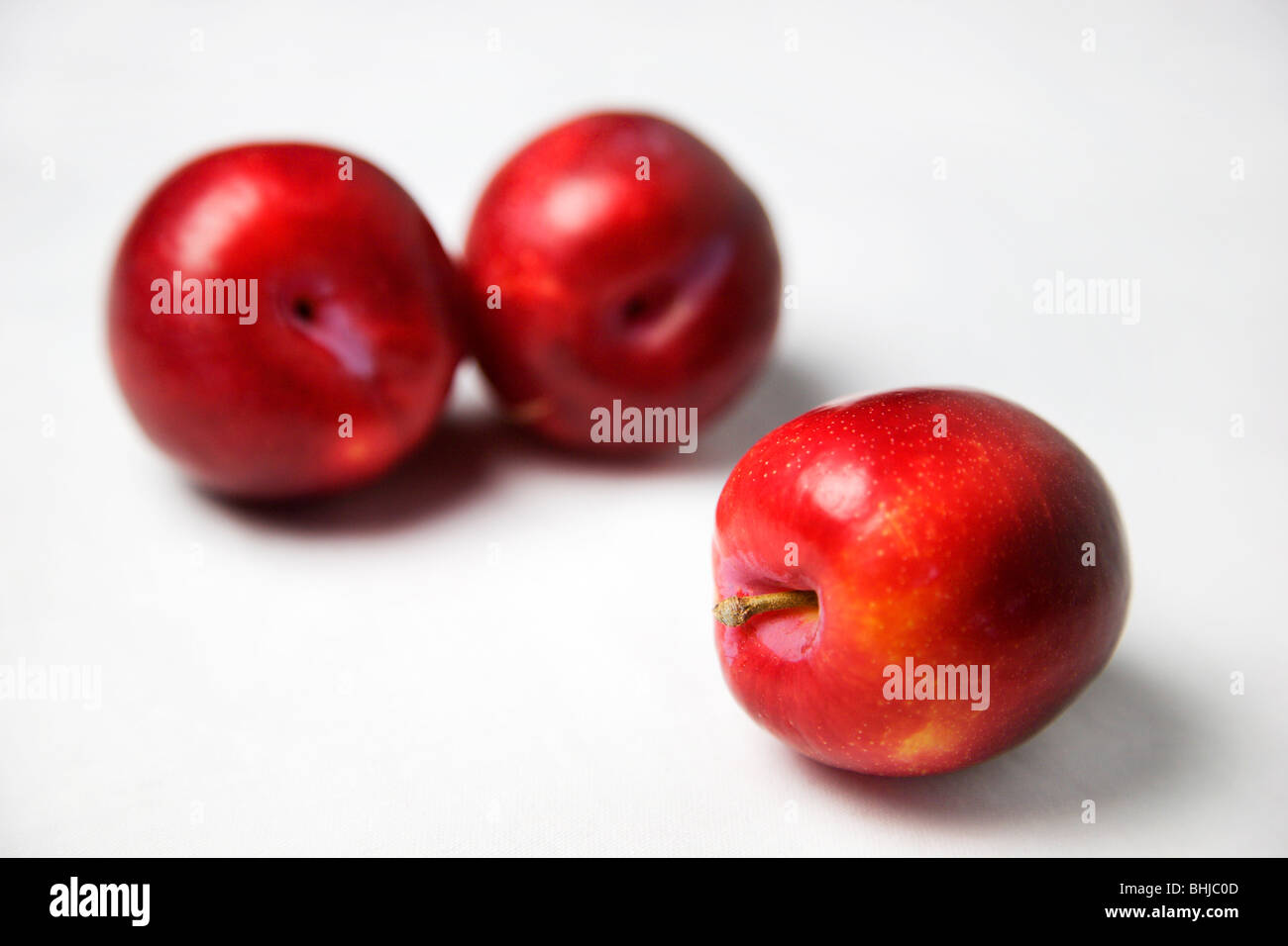 Trois prunes rouges sur un fond blanc Banque D'Images