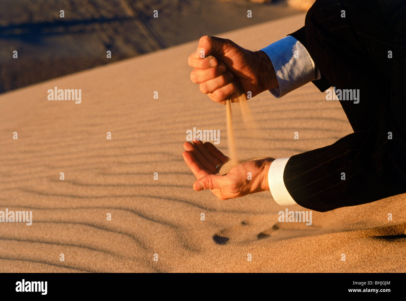 L'homme en costume d'affaires verser le sable du désert à travers ses mains, symbole du temps et de l'investissement et le changement calculé Banque D'Images