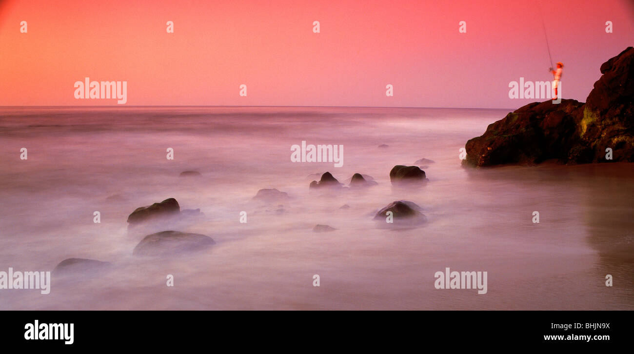 Pêcheur sur un rivage rocailleux au coucher du soleil à Laguna Beach, Californie Banque D'Images