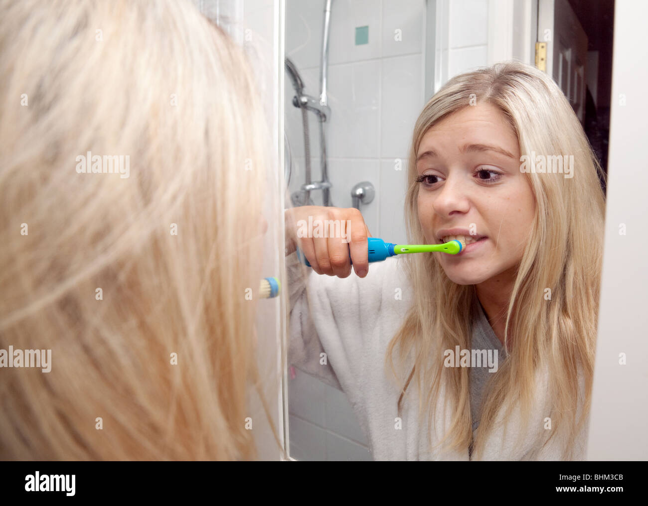 Adolescente blonde se brosser les dents avec une brosse à dents électrique reflète dans son miroir de salle de bains Banque D'Images