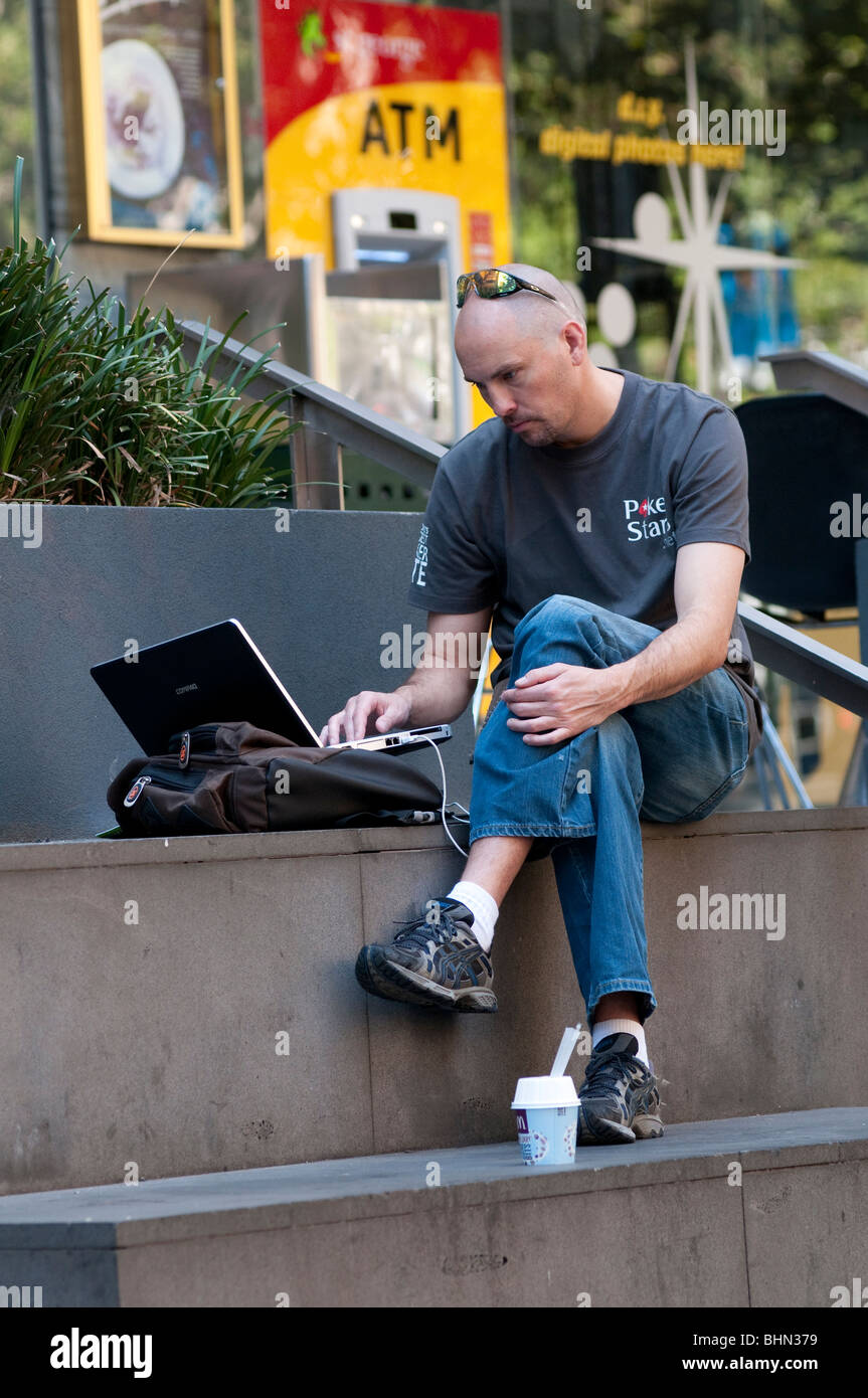 Man working on laptop à l'extérieur in city street Banque D'Images