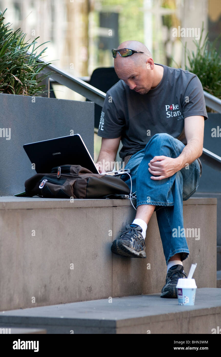 Man working on laptop à l'extérieur in city street Banque D'Images