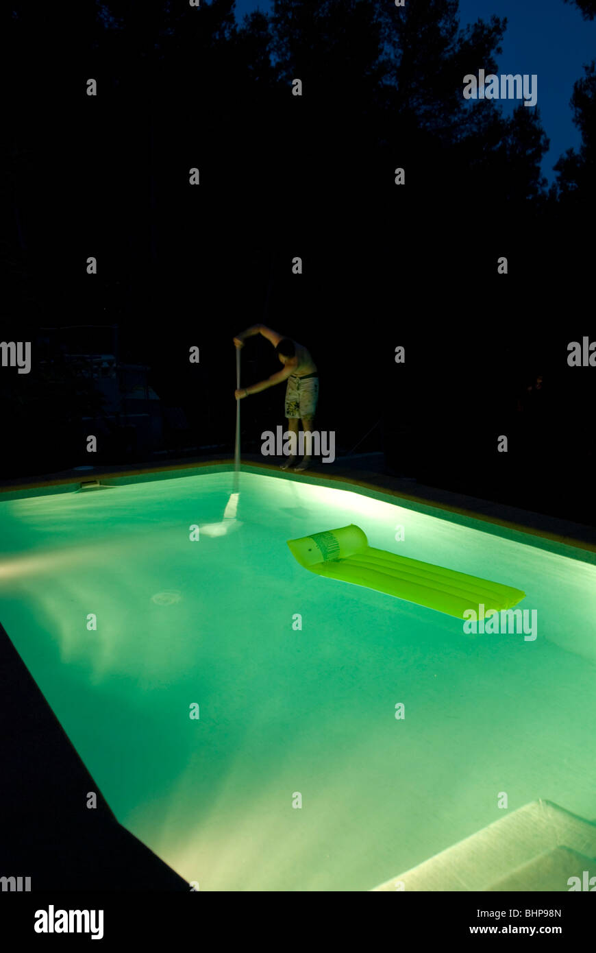 Vue d'un homme seul debout sur le bord d'une piscine la nuit allume la nettoyer à l'aide d'un filet Banque D'Images