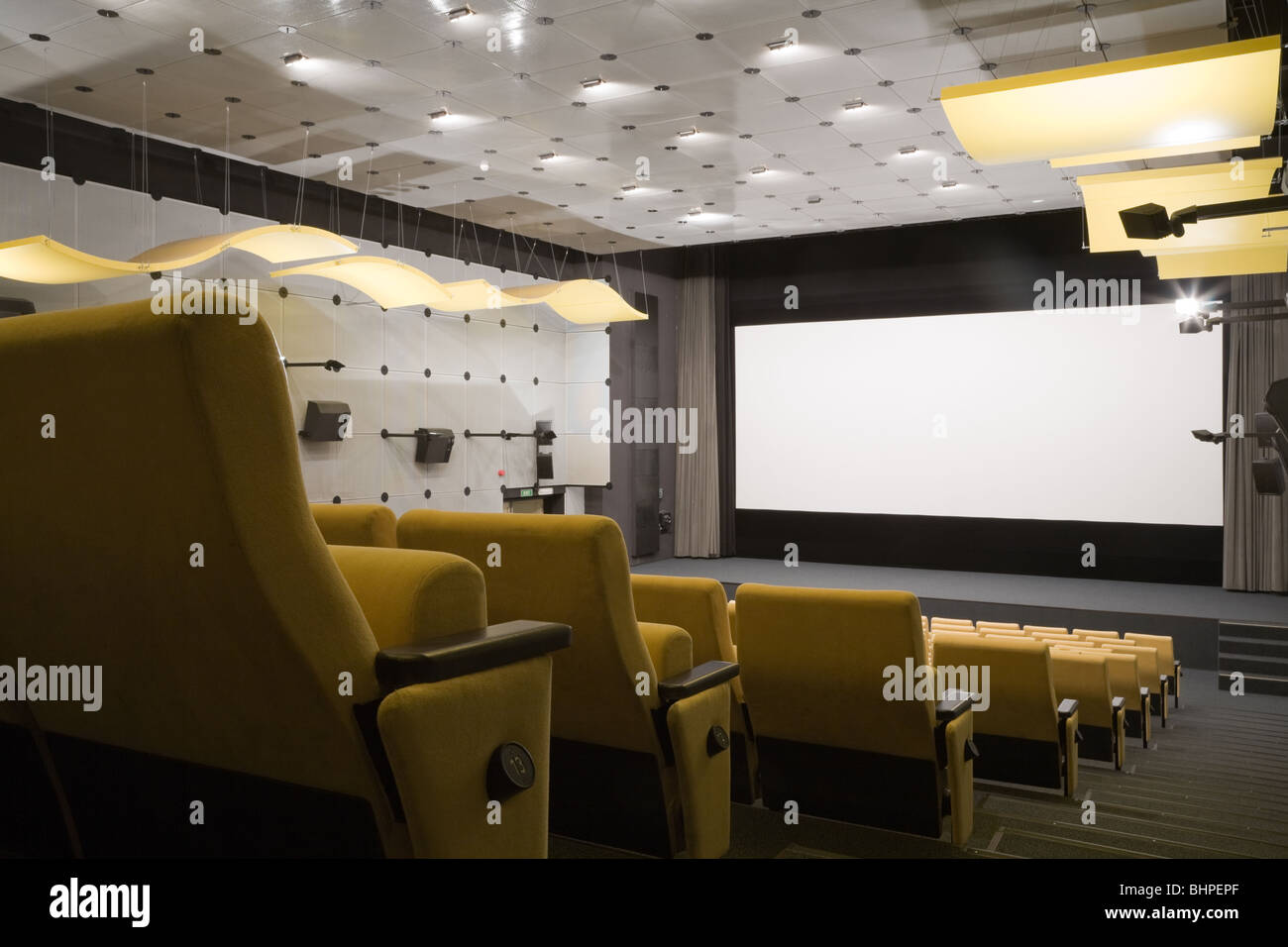 Salle de cinéma vide avec la ligne jaune de chaises, scène et écran de projection. Prêt pour l'ajout de votre propre photo. Banque D'Images